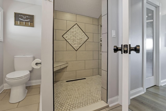 bathroom with hardwood / wood-style flooring, toilet, a textured ceiling, and a tile shower