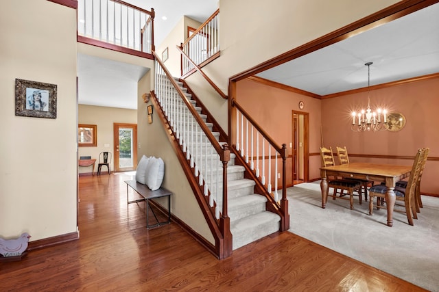 stairway with a towering ceiling, hardwood / wood-style flooring, an inviting chandelier, and crown molding