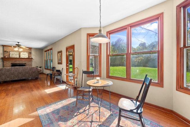 dining space with ceiling fan, wood-type flooring, and a brick fireplace