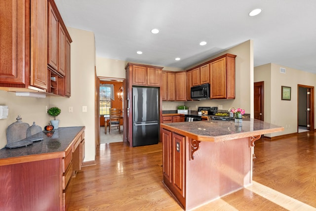 kitchen featuring a breakfast bar, kitchen peninsula, light hardwood / wood-style floors, and black appliances