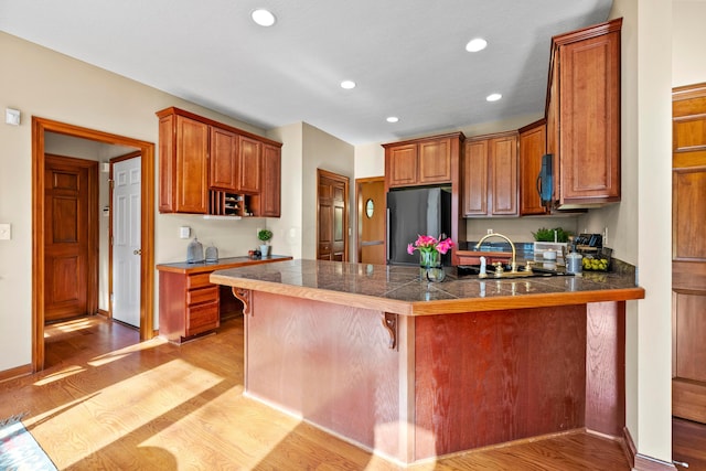 kitchen with a kitchen breakfast bar, light wood-type flooring, kitchen peninsula, and stainless steel refrigerator