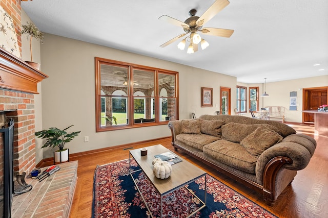 living room featuring hardwood / wood-style floors, ceiling fan, and a brick fireplace