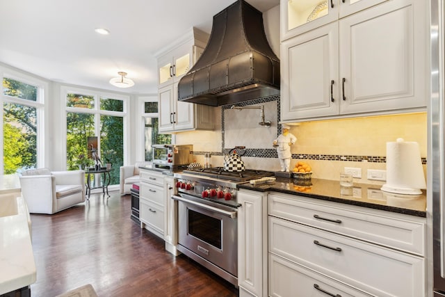 kitchen featuring white cabinetry, dark stone counters, decorative backsplash, premium stove, and custom range hood