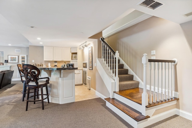 kitchen with a breakfast bar area, white cabinetry, white dishwasher, and light colored carpet