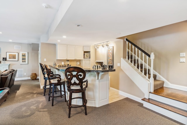 kitchen featuring a kitchen bar, white cabinetry, light carpet, and kitchen peninsula