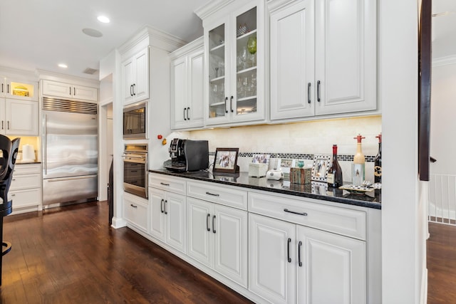 kitchen with white cabinetry, dark hardwood / wood-style flooring, dark stone counters, and built in appliances