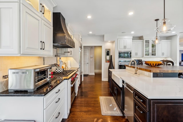 kitchen with white cabinetry, custom exhaust hood, hanging light fixtures, and built in appliances