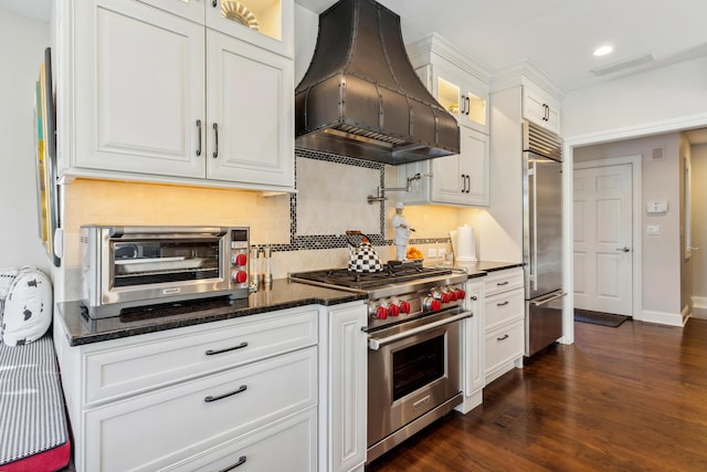 kitchen with premium range hood, premium appliances, decorative backsplash, dark stone counters, and white cabinets