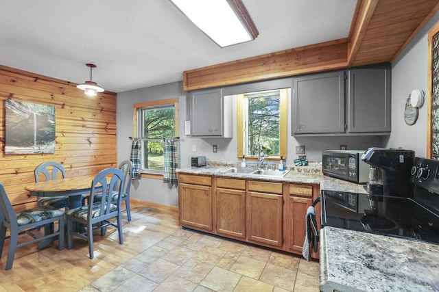 kitchen featuring light stone countertops, black appliances, sink, pendant lighting, and wood walls