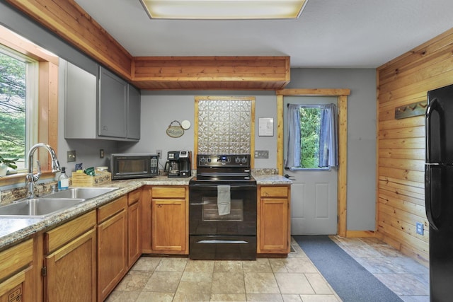 kitchen featuring black appliances, plenty of natural light, sink, and wooden walls