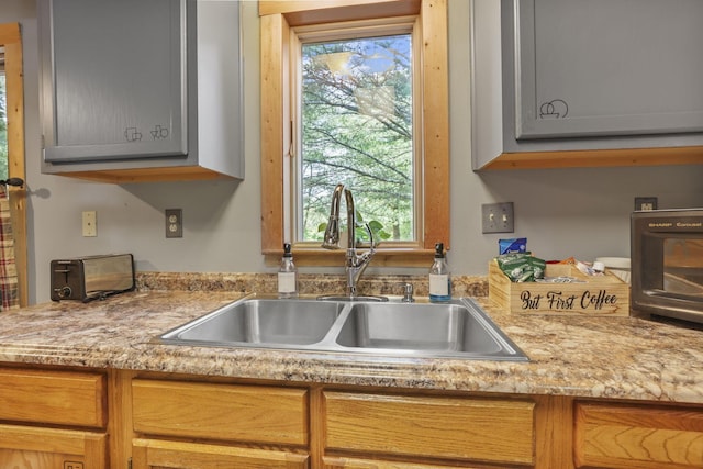 kitchen with light stone countertops, gray cabinetry, and sink