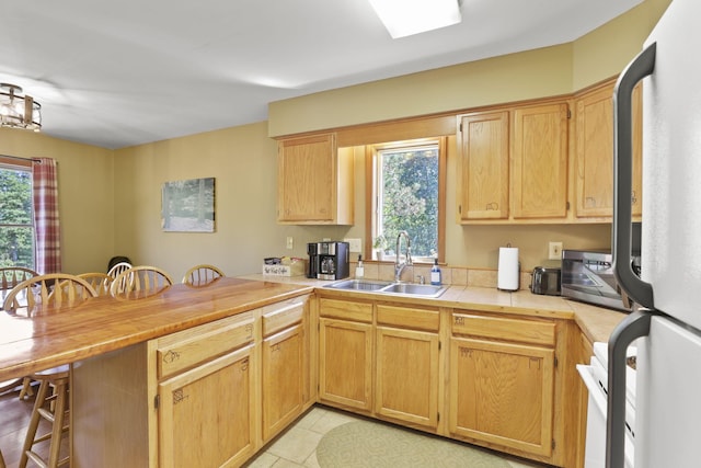 kitchen with white refrigerator, sink, light tile patterned flooring, kitchen peninsula, and a breakfast bar area