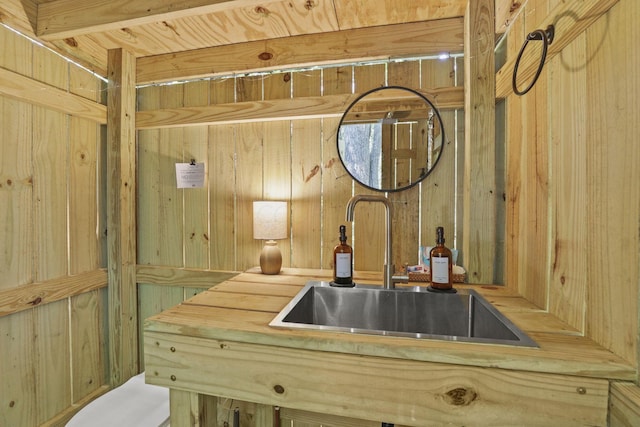 kitchen with wood walls, light brown cabinets, sink, and wooden counters