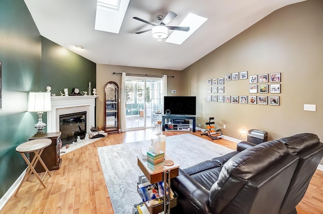 living room with light wood-type flooring, ceiling fan, and vaulted ceiling with skylight