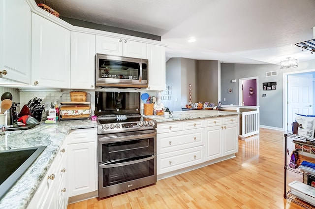 kitchen featuring appliances with stainless steel finishes, tasteful backsplash, light stone counters, light hardwood / wood-style flooring, and white cabinets