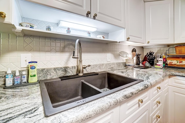 kitchen featuring light stone counters, tasteful backsplash, white cabinetry, and sink