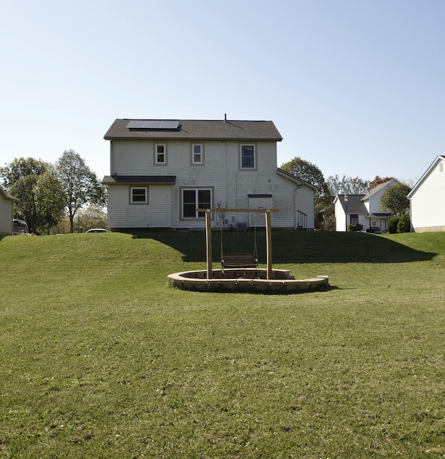 back of house with solar panels and a lawn