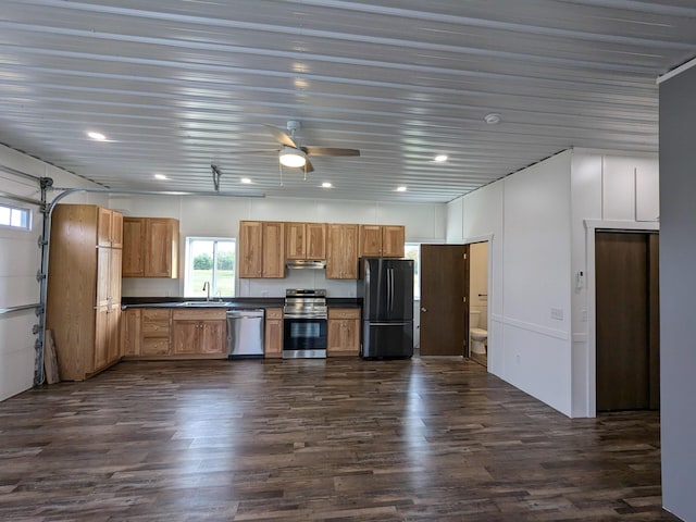 kitchen with dark wood finished floors, stainless steel appliances, dark countertops, a sink, and under cabinet range hood