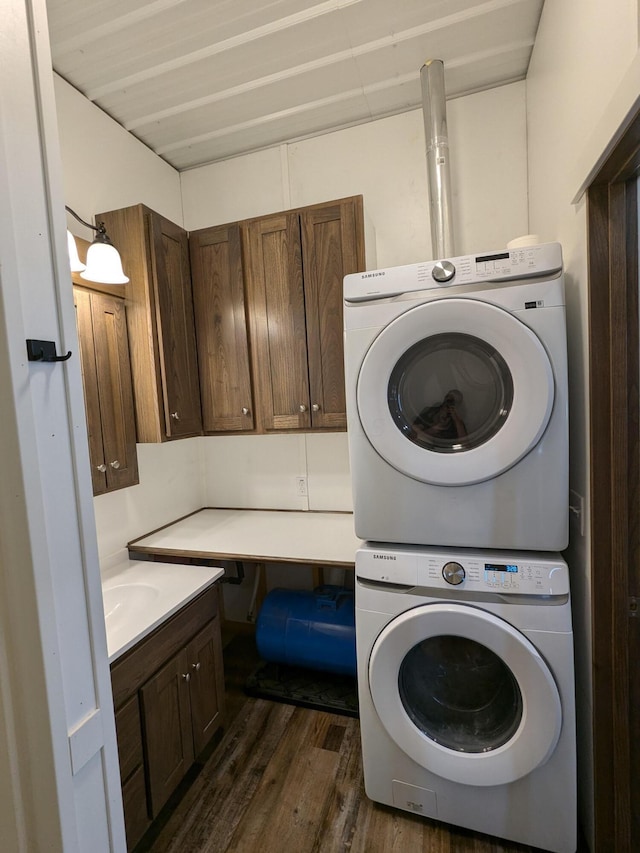 laundry area featuring cabinet space, dark wood finished floors, and stacked washer and clothes dryer