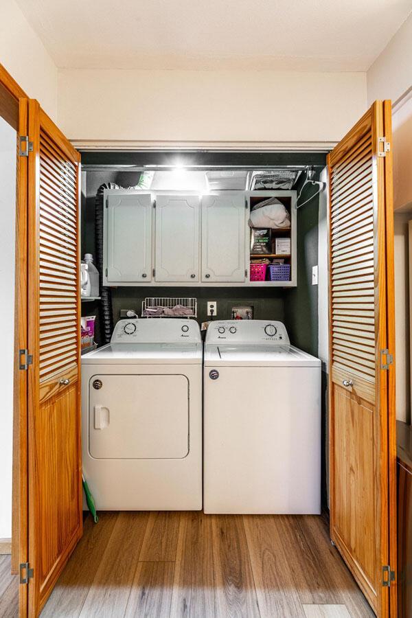 clothes washing area with cabinets, light wood-type flooring, and washing machine and dryer