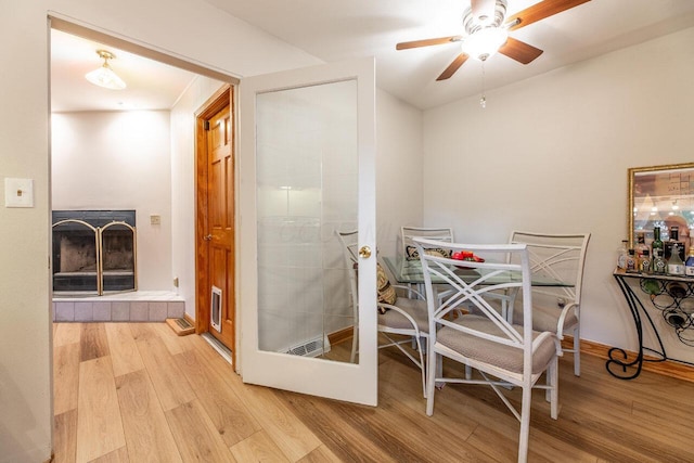 dining space with a tiled fireplace, ceiling fan, and light hardwood / wood-style flooring