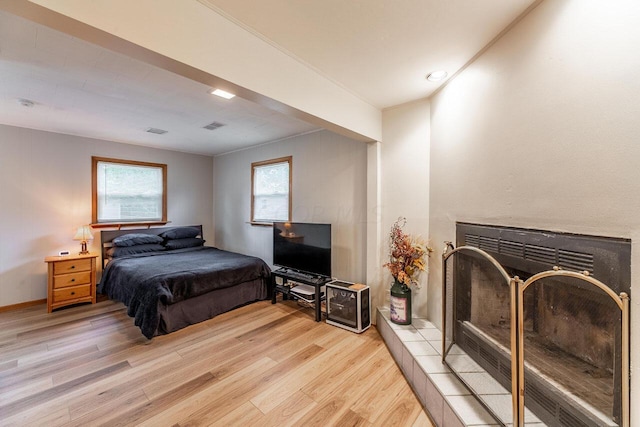 bedroom featuring light hardwood / wood-style flooring, crown molding, and a tiled fireplace