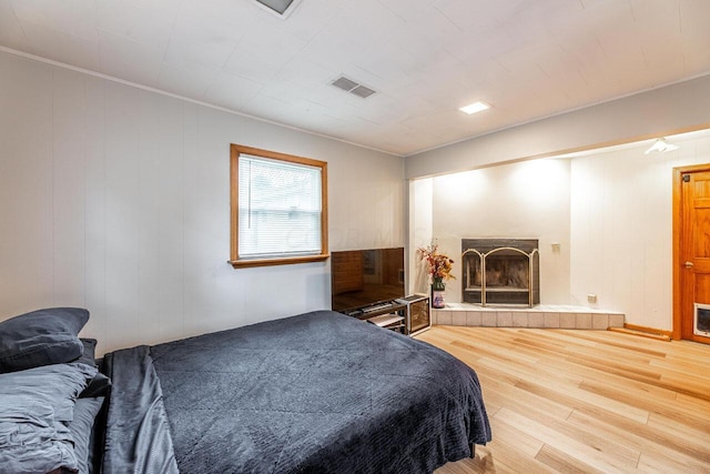 bedroom with hardwood / wood-style floors, crown molding, and a tiled fireplace