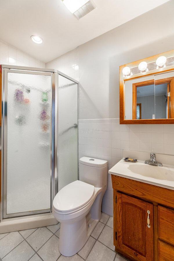 bathroom featuring toilet, a shower with door, tile patterned floors, and tile walls