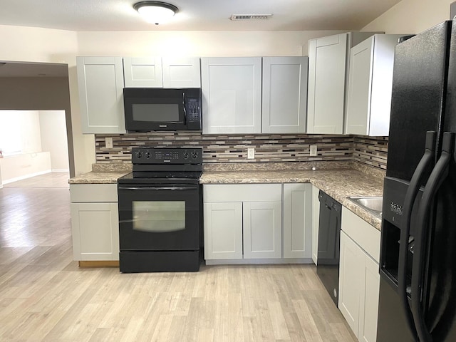 kitchen featuring light stone countertops, backsplash, black appliances, and light wood-type flooring