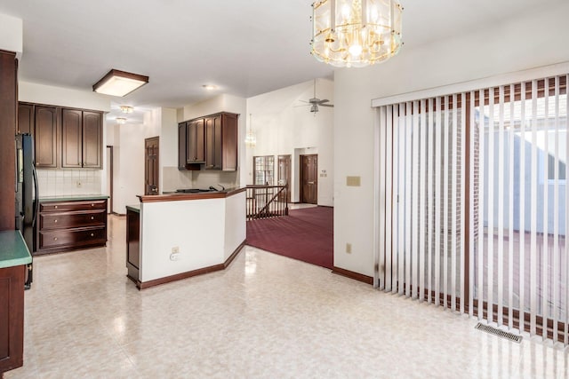 kitchen with black refrigerator, decorative backsplash, ceiling fan with notable chandelier, dark brown cabinetry, and decorative light fixtures