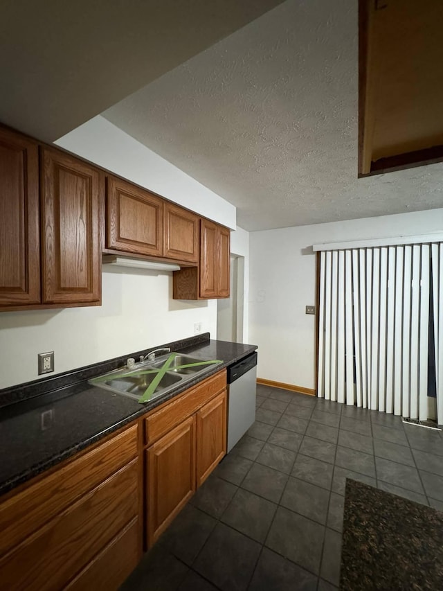 kitchen with dark tile patterned flooring, sink, stainless steel dishwasher, and a textured ceiling