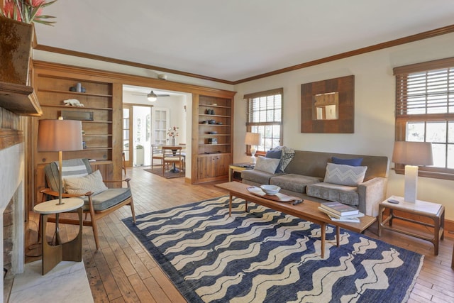 living room featuring a tile fireplace, light hardwood / wood-style flooring, built in features, and ornamental molding