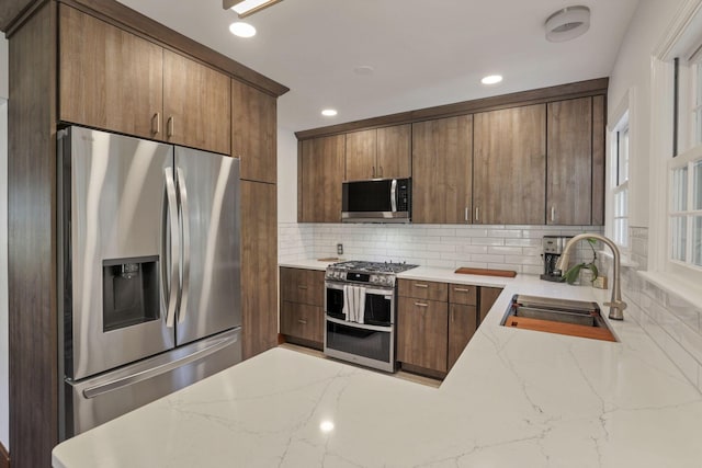 kitchen with decorative backsplash, sink, light stone counters, and stainless steel appliances