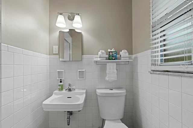 bathroom featuring toilet, tile walls, a sink, and a wainscoted wall