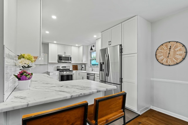 kitchen with dark wood finished floors, a peninsula, white cabinets, appliances with stainless steel finishes, and decorative backsplash