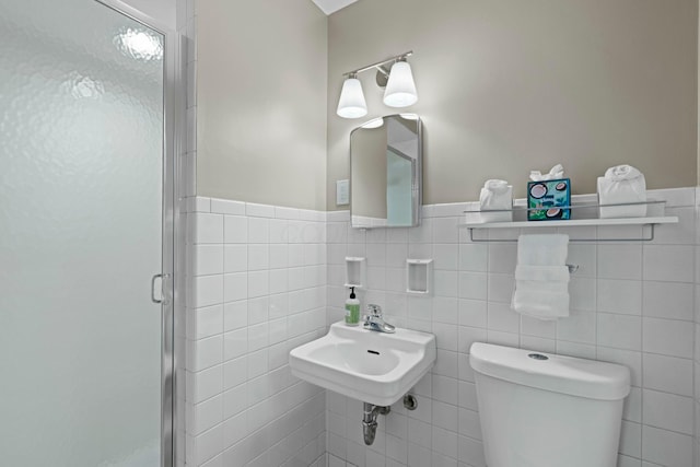 bathroom featuring a stall shower, toilet, a wainscoted wall, tile walls, and a sink