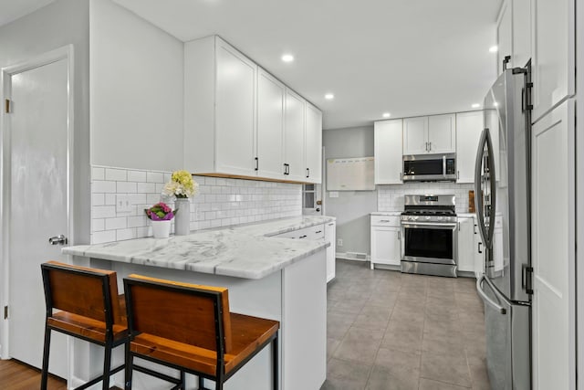 kitchen featuring recessed lighting, white cabinetry, backsplash, light stone countertops, and stainless steel appliances