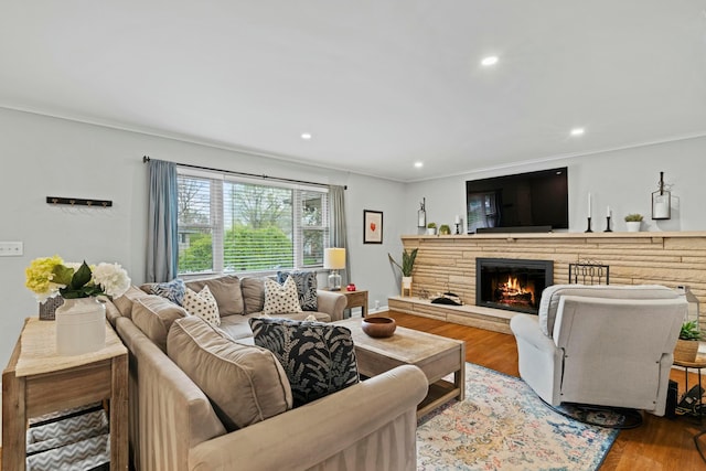 living room featuring recessed lighting, a stone fireplace, ornamental molding, and wood finished floors