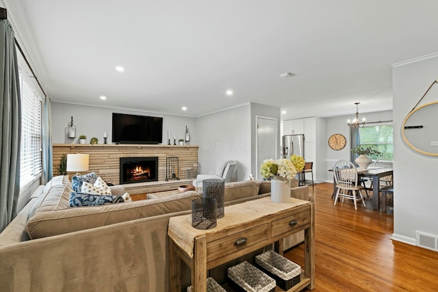 living room featuring light wood-type flooring, a stone fireplace, visible vents, recessed lighting, and a notable chandelier