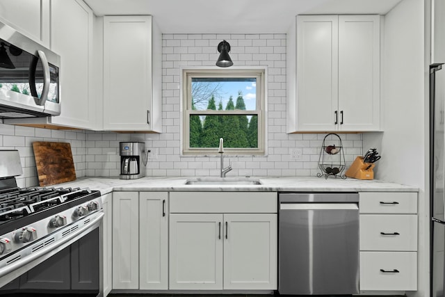 kitchen featuring a sink, backsplash, appliances with stainless steel finishes, and white cabinetry
