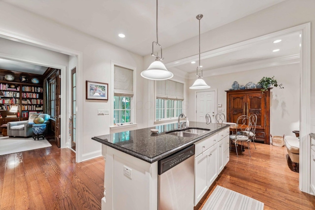 kitchen featuring a kitchen island with sink, white cabinets, sink, stainless steel dishwasher, and decorative light fixtures