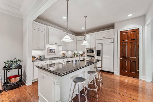 kitchen with sink, built in appliances, light wood-type flooring, an island with sink, and white cabinetry