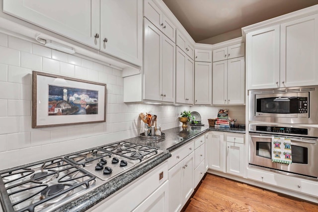 kitchen with stainless steel appliances, dark stone countertops, light hardwood / wood-style floors, decorative backsplash, and white cabinets