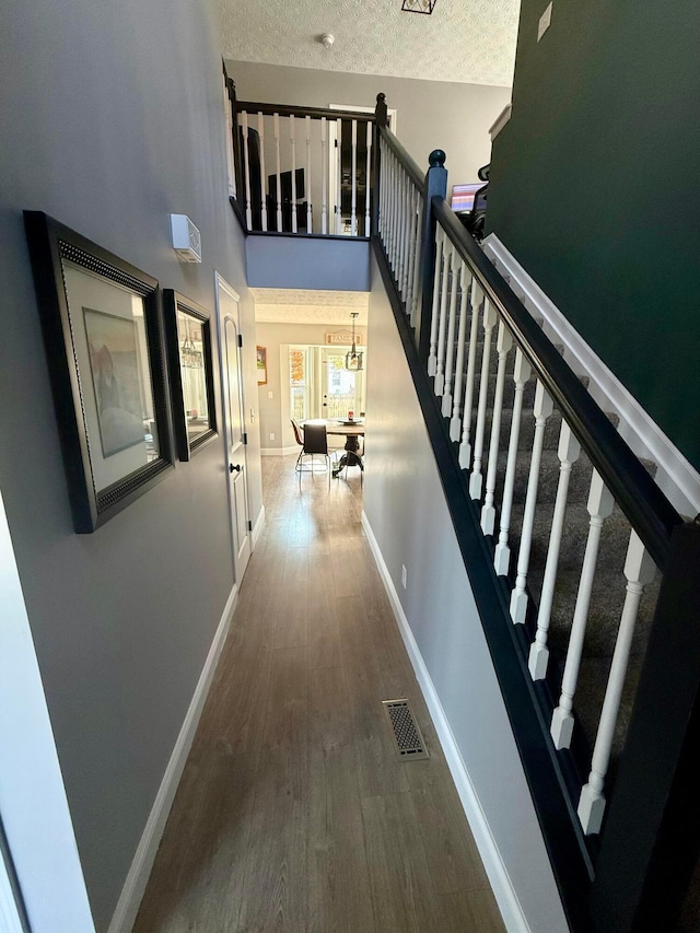 corridor featuring a high ceiling, wood-type flooring, and a textured ceiling