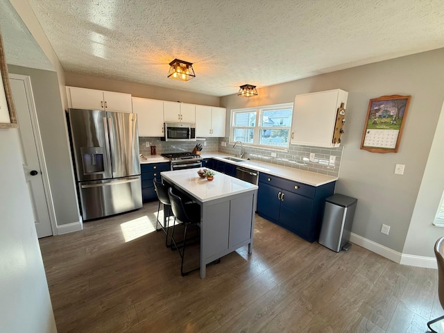 kitchen featuring appliances with stainless steel finishes, a breakfast bar, blue cabinetry, white cabinets, and a center island