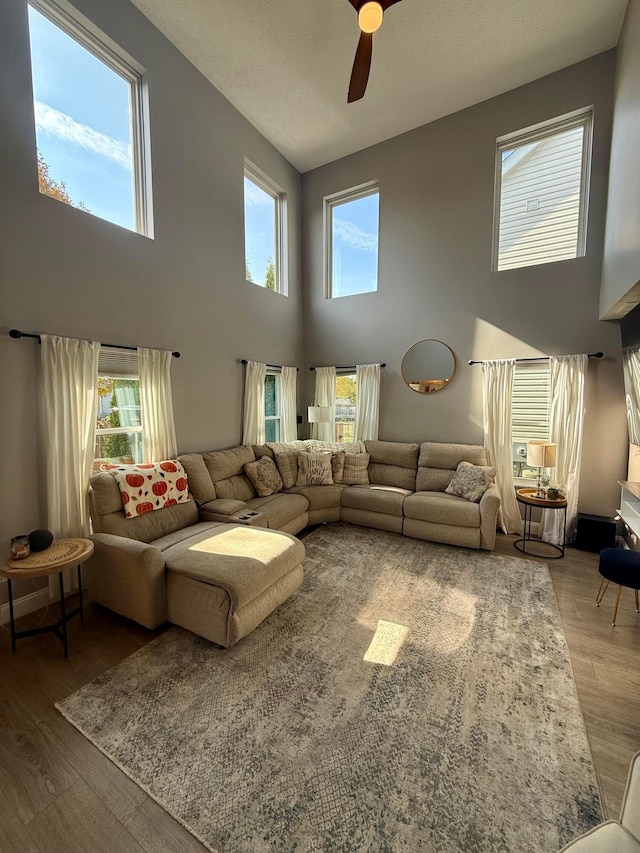 living room with ceiling fan, plenty of natural light, a towering ceiling, and hardwood / wood-style flooring