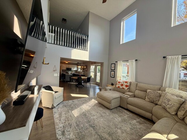 living room with a towering ceiling, hardwood / wood-style flooring, ceiling fan, and a healthy amount of sunlight