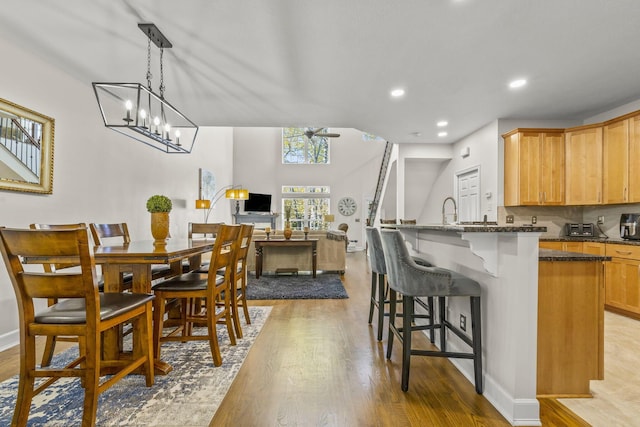 kitchen featuring dark stone counters, ceiling fan with notable chandelier, sink, pendant lighting, and light hardwood / wood-style floors