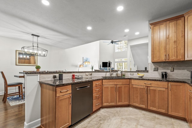 kitchen with dishwasher, dark stone counters, hanging light fixtures, sink, and ceiling fan