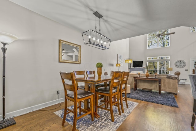 dining room featuring ceiling fan with notable chandelier, wood-type flooring, and a high ceiling